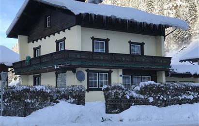 A charming house in the alpine style, surrounded by snow. The amount of snow on the roof is impressive, and the landscape is peaceful.