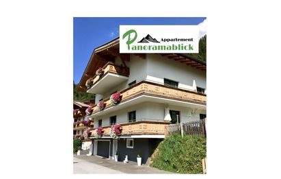 Ein modernes Appartementhaus mit Balkonen und blühenden Blumen. Das Logo "Appartement Panoramablick" ist deutlich sichtbar.