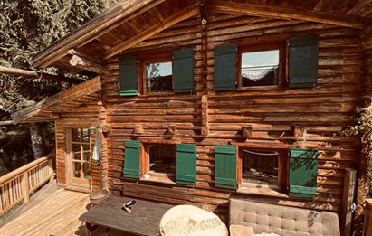A cozy wooden house with green shutters. The outdoor area features a terraced wooden deck.