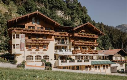 Ein charmantes Hotel im alpine Stil, umgeben von grünen Wäldern. Die Fassade ist mit Holzverkleidungen und Balkonen geschmückt.