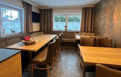 A cozy dining area with wooden furniture and comfortable chairs. Large windows provide plenty of daylight.