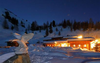 A picturesque mountain cottage in the snowy landscape at night. Soft light shines from the windows and illuminates the winter dream.