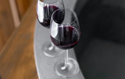 Zwei Weingläser mit rotem Wein stehen an den Rändern eines Whirlpools. Im Hintergrund ist eine Holzstruktur sichtbar.