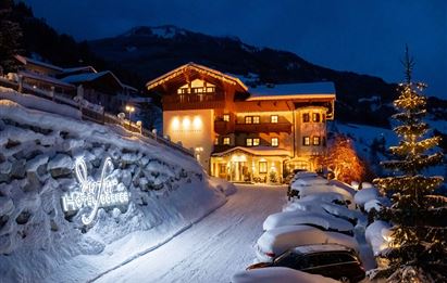 Ein wunderschönes Hotel in den Bergen, umgeben von Schnee. Die Fassade ist stimmungsvoll beleuchtet und der Wintergarten schafft eine einladende Atmosphäre.