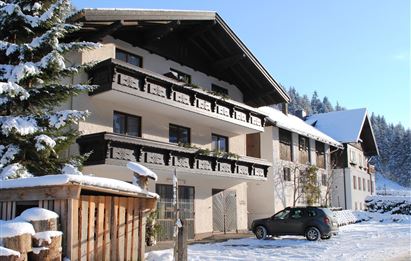 A cozy building in the snow, surrounded by spruce trees. The sky is clear and the sun is shining on the winter landscape.