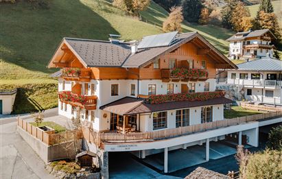 A beautiful chalet with wooden cladding and balcony flowers. Surrounded by green hills and a peaceful landscape.
