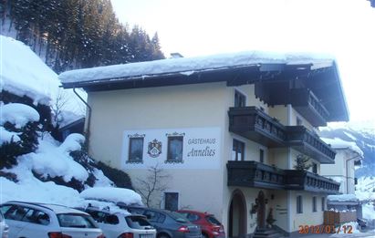 Ein malerisches Gästehaus im Winter mit schneebedecktem Dach. Vor der Unterkunft sind mehrere Autos geparkt, umgeben von einer wunderschönen, verschneiten Landschaft.