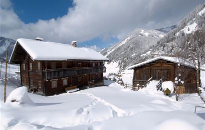 Eine malerische Winterlandschaft mit schneebedeckten Hütten. Im Hintergrund sind schneebedeckte Berge und ein blauer Himmel zu sehen.
