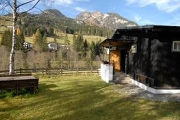 Ein gemütliches Chalet in der Natur mit Blick auf die Berge. Der Garten ist grün, und in der Nähe gibt es einen kleinen Tisch.