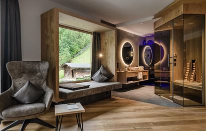 Ein modernes Zimmer mit großen Fenstern und einer gemütlichen Sitzecke. Die Sauna ist ebenfalls gut sichtbar und fügt dem Raum eine entspannende Atmosphäre hinzu.