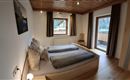 A modern bedroom with two single beds and bright wooden elements. Large windows let in plenty of natural light and offer a view outside.