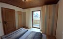 A cozy bedroom with a double bed and wooden ceiling. A window provides access to a balcony with an outdoor view.