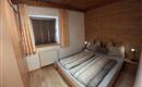 A cozy bedroom with a double bed and wood paneling. Large windows with curtains let in plenty of light.