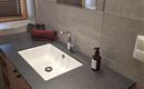 A modern bathroom with an elegant sink and wooden base. On the surface are a soap dispenser and a towel.