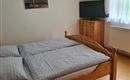 A simple bedroom with a double bed and two pillows.  
A picture is hanging on the wall, and a television is standing on a wooden cabinet.
