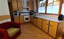 A bright kitchen with wooden cabinets and large windows. A red sofa is positioned in the corner next to the kitchenette.