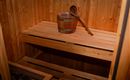 A cozy sauna with wooden shelves and a wooden container. A wooden spoon is also lying beside it.