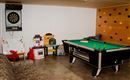 A room with a billiard table and a dartboard on the wall. There are also toys and a climbing wall.