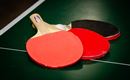 Three table tennis paddles are lying on a green table tennis field. Two paddles are red and one is black.