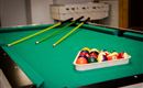 A billiard table with green felt and three cue sticks. A bowl of colorful billiard balls is on the table.