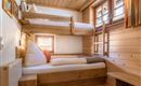 A cozy bedroom with a wooden loft bed and a lower bed. The room has warm wooden paneling and a window with a view outside.