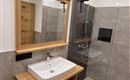 A modern bathroom with a clear shower and a ceramic sink. The walls are in neutral gray tones, and a wooden shelf complements the design.