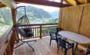 Eine gemütliche Terrasse in den Bergen mit einem Hängesessel und einem Tisch mit Stühlen. Der Ausblick zeigt die umliegende Landschaft und Täler.