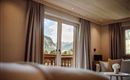 A cozy room with large windows and a view of the mountains. The decor is modern and bright, with soft colors.