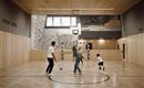An interior space with a sports field where four people are playing soccer. The walls are decorated with climbing elements and large windows provide light.