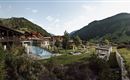 A picturesque landscape with a swimming pool and modern buildings. Gentle hills and a clear sky frame the scene.
