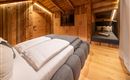 Ein gemütliches Schlafzimmer mit Holzwänden und einem modernen Bett. Im Hintergrund befindet sich eine sitzecke mit Kissen.