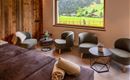 Ein modernes Wohnzimmer mit komfortablen Sesseln und einem großen Fenster. Durch das Fenster ist die grüne Landschaft der Alpen sichtbar.