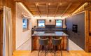 Eine moderne Küche mit Holzdecken und eleganten, grauen Schränken. Eine gemütliche Bar mit zwei Stühlen ergänzt den offenen Raum.