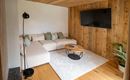 Ein moderner Wohnraum mit hellem Holz und einer gemütlichen Couch. An der Wand befindet sich ein Fernseher und eine Pflanze sorgt für einen frischen Akzent.