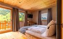 Ein gemütliches Schlafzimmer mit Holzdecke und großen Fenstern. Der Ausblick zeigt eine grüne Landschaft mit Bergen.