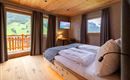Ein gemütliches Schlafzimmer mit Holzwänden und großen Fenstern. Der Blick zeigt eine grüne Landschaft und eine moderne Einrichtung.