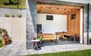 Ein gemütlicher Außenbereich mit Holzmöbeln und einem modernen, offenen Design. Die Terrasse ist von geräumigen Wänden aus Stein umgeben und lädt zum Entspannen ein.