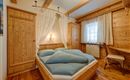 A cozy wooden bedroom with a large bed and blue bedding. The decor is rustic and inviting, featuring a window and a chair.