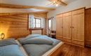 A cozy bedroom with wooden paneling and a large bed. There is a wardrobe and a window with curtains.
