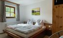 Ein gemütliches Schlafzimmer mit einem großen Bett und weichen Bettdecken. Ein Fenster lässt Tageslicht herein, und an der Wand hängt ein Landschaftsgemälde.
