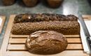 Drei verschiedene Brote auf einem Holzbrett. Zwei langgestreckte Brote und ein rundes Brot in der Mitte.