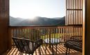 Ein Balkon mit zwei gemütlichen Stühlen und einem Tisch. Im Hintergrund sind die Berge und die aufgehende Sonne zu sehen.