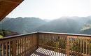Eine sonnige Aussicht vom Balkon auf die Berge. Die Landschaft ist grün und hügelig, mit strahlendem Licht im Hintergrund.