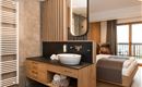 Ein modernes Badezimmer mit einem eleganten Waschbecken und Holzdetails. Im Hintergrund ist ein gemütliches Schlafzimmer mit Fenster und einem Balkon sichtbar.