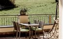 Ein gemütlicher Balkon mit einem Tisch und Stühlen. Im Hintergrund sieht man eine grüne Wiese und einen hängenden Stuhl.
