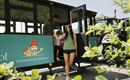 A family is getting off a bus with a cheerful design. In the background, a tractor and a garden landscape can be seen.