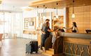 A family checks in at the reception of a hotel. The reception area is furnished in a modern and bright way.