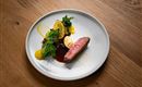 An elegant dish on a white plate. It consists of tender meat, fresh vegetables, and a side of fruit puree.