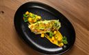 An artistic dish on a black plate. It consists of sushi, broccoli, and fresh mango.