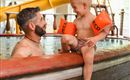 A father and his son are playing together in the water. The boy is wearing swim floaties and is smiling happily.